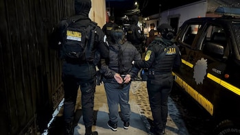Agentes uniformados escoltan a una mujer esposada por la espalda en una calle de noche junto a una camioneta policial