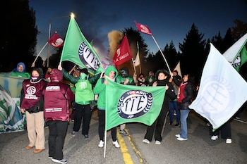 Grupo de personas manifestándose con banderas verdes y bordó de ATE y una pancarta de "100 AÑOS ATE" en una carretera al anochecer, con árboles al fondo