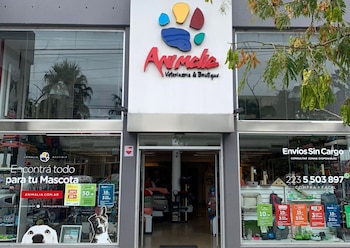 Fachada de la veterinaria y boutique Animalia con ventanales que exhiben productos para mascotas, un cartel luminoso con logo de huella de pata y promociones
