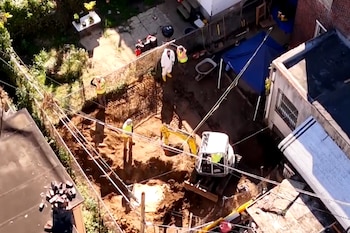 Vista aérea de varias personas y una pequeña excavadora que remueven tierra en el patio trasero cercado de una casa