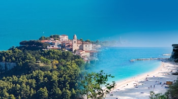 Composición fotográfica de un pueblo en una colina arbolada a la izquierda y una playa de arena con personas a la derecha.
