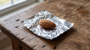 Una almendra sobre un trozo de papel de aluminio arrugado descansa en una mesa de madera oscura cerca de una ventana.
