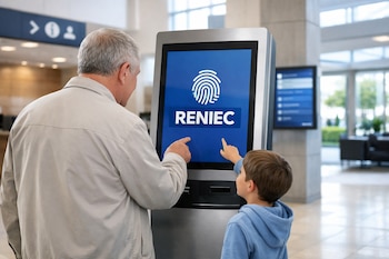 Un hombre de espaldas y un niño de perfil apuntan a la pantalla de un tótem digital con el logo de Reniec en un vestíbulo moderno.