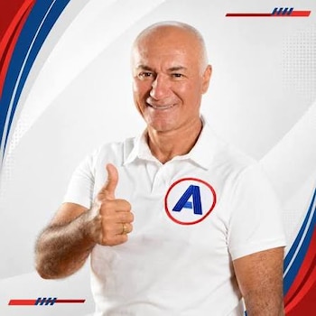 Retrato de un hombre sonriente con camisa polo blanca con el logotipo de una letra A, que realiza el gesto de pulgar hacia arriba