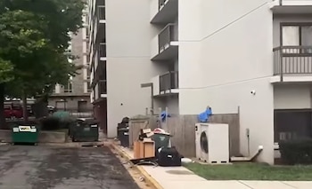 Parte trasera de un edificio residencial con balcones, contenedores de basura y objetos acumulados junto a una acera