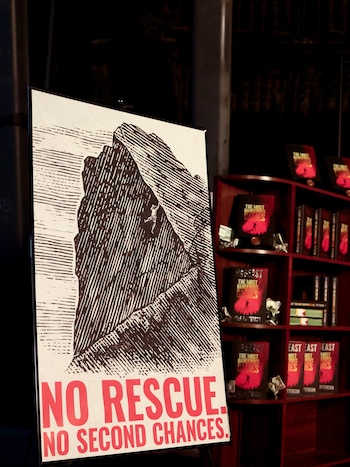 Un cartel con la ilustración de un escalador en una montaña junto a una estantería de madera con libros de MrBeast