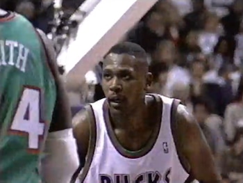 Primer plano de Glenn Robinson con uniforme blanco y otro jugador con uniforme verde y el número cuatro. Público borroso al fondo