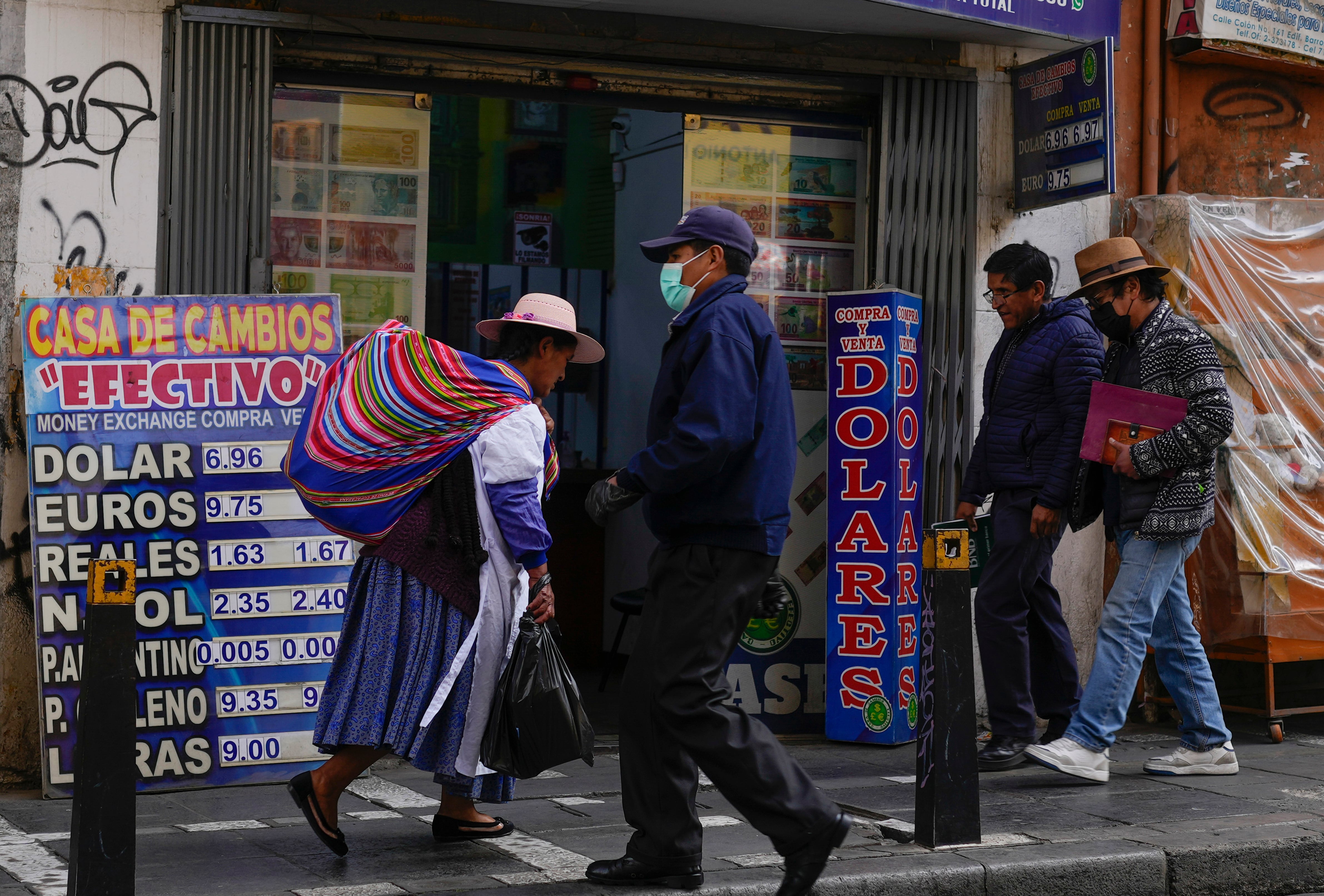 ARCHIVO - Peatones caminan junto a una tienda de cambio de moneda en La Paz, Bolivia, el 12 de junio de 2024. Con el incremento de los precios, la escasez de dólares y las filas en gasolineras faltas de combustible, las protestas en Bolivia se han incrementado por la crisis económica. (AP Foto/Juan Karita, Archivo)