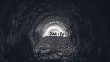 Grupo de personas con cascos y chalecos reflectantes de pie sobre escombros dentro de un túnel oscuro, silueteadas por una intensa luz al final
