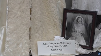 Fotografía en blanco y negro de una novia sonriente con velo y vestido de encaje, un vestido de novia de encaje y un cartel con nombres y fecha