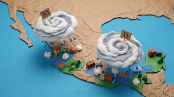Mapa de México de cartón con dos nubes espiraladas con números 10 y 11, gotas de lluvia, casas y árboles en miniatura sobre un fondo azul.