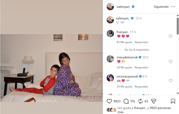 Una mujer y un niño con pijama están sentados espalda con espalda sobre una cama hecha con sábanas blancas