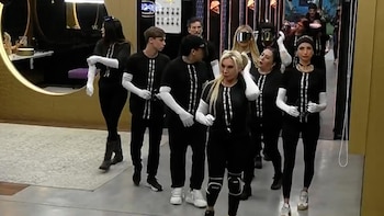 Un grupo de personas vestidas con ropa negra, mangas y guantes blancos camina por el interior de una vivienda