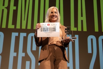 Mercedes Morán sonríe luciendo un traje de dos piezas marrón claro mientras sostiene un diploma de reconocimiento y una estatuilla transparente