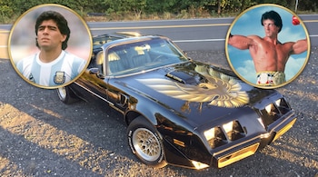 Un automóvil negro Pontiac Trans Am estacionado junto a dos círculos con las figuras de Diego Maradona y Rocky Balboa.