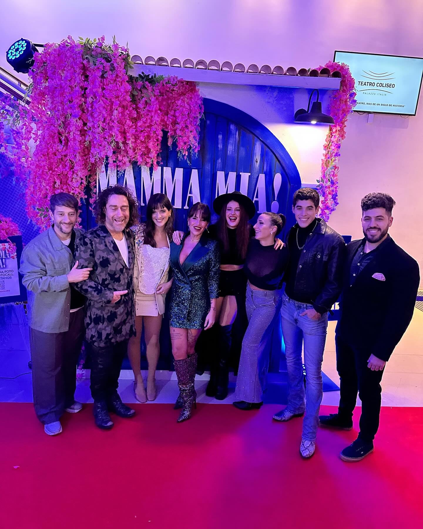 Un grupo de ocho actores de la obra Mamma Mia posa sonriente sobre una alfombra roja
