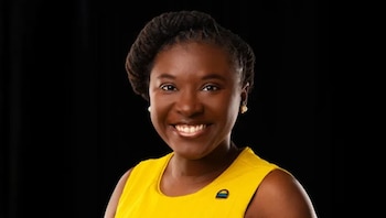 Retrato de una mujer sonriente con piel oscura, cabello oscuro recogido y un vestido amarillo, sobre un fondo negro liso