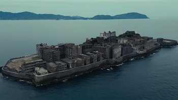 Vista aérea de la isla Hashima, Japón, cubierta por numerosos edificios de hormigón grises y abandonados. La isla está rodeada por el mar con montañas al fondo