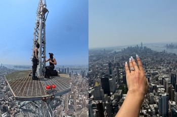 Dos personas vestidas de negro y con rostros cubiertos en una plataforma metálica elevada, una arrodillada. Mano con anillo y manicura en primer plano. Ciudad al fondo