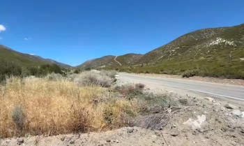 Carretera asfaltada junto a matorrales secos y montañas bajo un cielo despejado