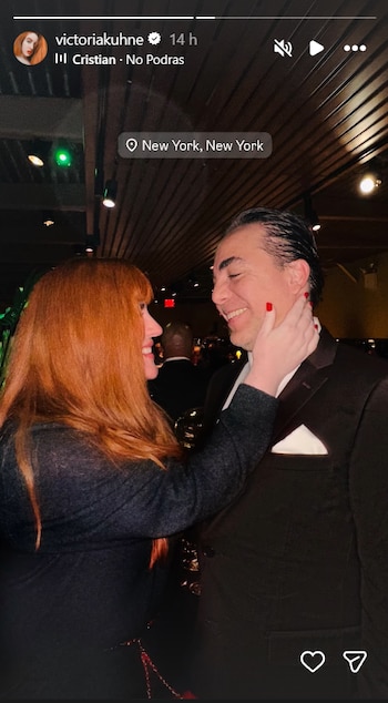 Vistoria Künhe, mujer de cabello rojizo, sonríe a Cristian Castro, quien también sonríe. La mano de ella, con uñas rojas, toca la mandíbula de él