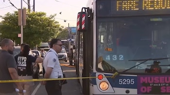 Agentes del NYPD inspeccionan un autobús de servicio turístico en una calle acordonada con cinta amarilla de la escena del crimen durante el día