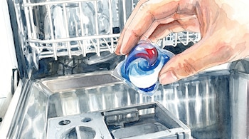 Una mano inserta una cápsula de detergente azul, roja y blanca en el dispensador de un lavavajillas. Se observan las rejillas del aparato.