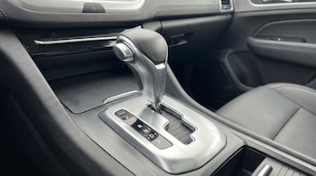 Primer plano de la palanca de cambios plateada y negra de un auto automático, mostrando las posiciones P, R, N, D y 2, con el interior oscuro del vehículo.