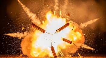 Varias barras de dinamita con mechas rodeadas por una gran explosión de fuego, humo y chispas incandescentes.