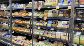 Refrigerador de supermercado con múltiples estantes; paquetes de queso lácteo y rebanadas, así como numerosas alternativas vegetales sin lácteos.