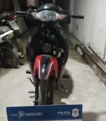 Una motocicleta roja y negra sin su carenado delantero se encuentra estacionada detrás de un cartel de la Policía de la Provincia de Buenos Aires