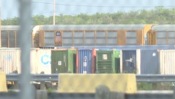 Vagones de tren amarillos de Union Pacific, texto "Building America", detrás de contenedores de carga blancos, verdes, azules, rojos y grises