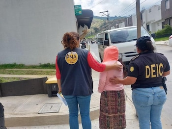 Vista trasera de dos agentes, una con chaleco PNA y otra con uniforme DEIC, flanqueando a una persona con sudadera rosa y falda en una acera