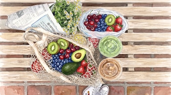 Vista superior de un banco de madera con una bolsa de frutas variadas, dos bebidas en vasos plásticos, flores y un periódico doblado.