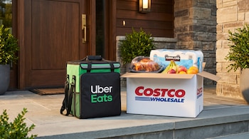 Una bolsa verde de reparto de Uber Eats junto a una caja de Costco con frutas, pollo y papel higiénico en el porche de una casa.