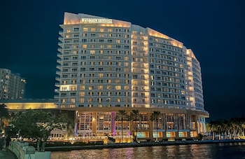 Un rascacielos blanco de varios pisos con el letrero 'Mandarin Oriental' iluminado en la cima, reflejándose en el agua con palmeras