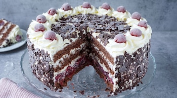 Tarta Selva Negra con una rebanada cortada, mostrando capas de bizcocho de chocolate, crema blanca y cerezas. Está decorada con chocolate y cerezas escarchadas.