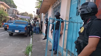 Vista lateral de agentes de seguridad con cascos y chalecos tácticos junto a camionetas pickup azules en una calle con edificios