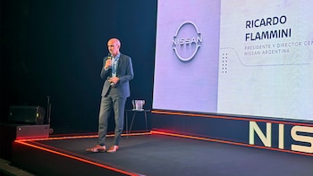Un hombre con traje habla por micrófono en un escenario junto a una pantalla con el logotipo de Nissan y el texto Ricardo Flammini