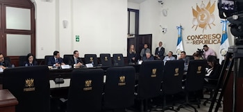 Personas con vestimenta formal en una mesa de reuniones junto a banderas y la insignia del Congreso de la República
