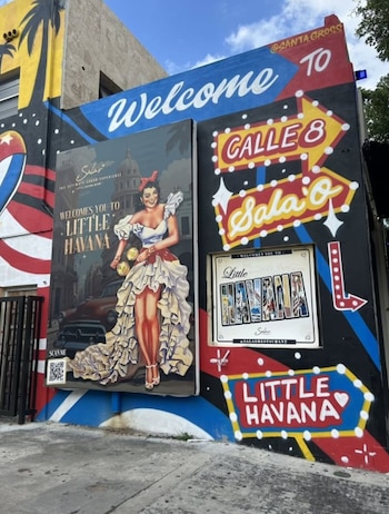 Mural exterior con signos de "Welcome to Calle 8" y "Little Havana", y una ilustración de una mujer vestida con un traje de volantes