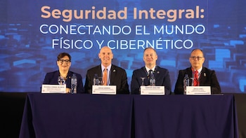 Cuatro personas, tres hombres y una mujer, sentadas detrás de una mesa azul oscuro. Detrás, una pantalla muestra "Seguridad Integral"