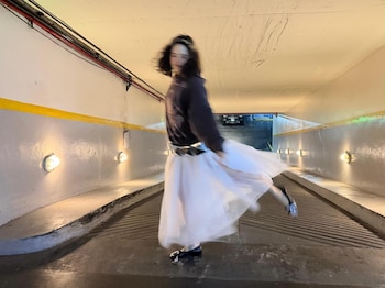 Rosalía, borrosa por el movimiento, baila en una rampa de cemento con paredes blancas y franja amarilla, bajo luces industriales