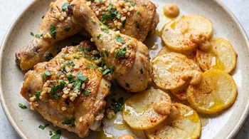 Plato con presas de pollo doradas, ajo picado, perejil fresco y rodajas de papa con pimentón, aceite y gotas de salsa cremosa.