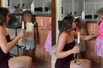 Mujer con gafas sosteniendo una vela encendida, dos niñas con caras difuminadas junto a gabinetes de cocina en un interior
