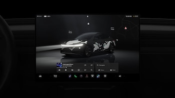 Pantalla táctil que muestra un automóvil negro digitalizado con figuras de fantasmas blancos y murciélagos, junto a controles de navegación y audio