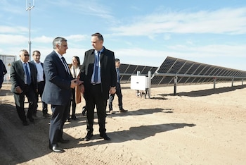 Manuel Adorni e Alfredo Cornejo, com Horacio Marín e comitiva, conversando sobre um campo arenoso com uma fileira de painéis solares e um céu claro ao fundo.