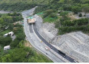 Una vista aérea de una carretera de dos sentidos con un túnel, maquinaria pesada en una zona de excavación y árboles a los lados