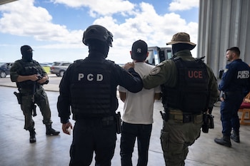 Cinco hombres, tres con uniformes tácticos y pasamontañas, uno con camiseta blanca y gorra, y otro con uniforme azul de Fuerza Pública. Chalecos con las letras PCD y UCE.