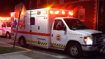 Dos ambulancias blancas del departamento de bomberos, con luces de emergencia rojas y naranjas encendidas, estacionadas en la calle de noche